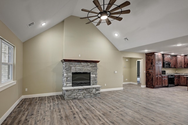unfurnished living room featuring light wood-type flooring, visible vents, a stone fireplace, and a ceiling fan