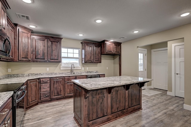kitchen with black appliances, a kitchen breakfast bar, light wood-type flooring, and a sink