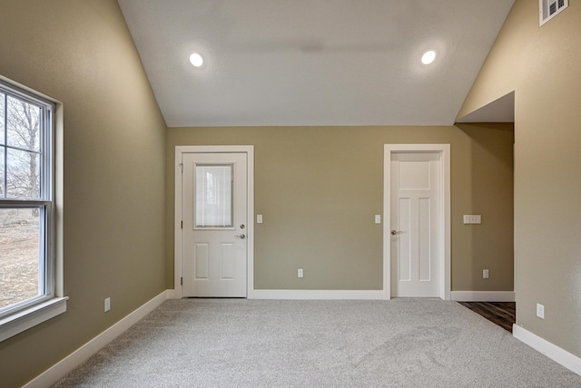 carpeted empty room with plenty of natural light, visible vents, baseboards, and lofted ceiling