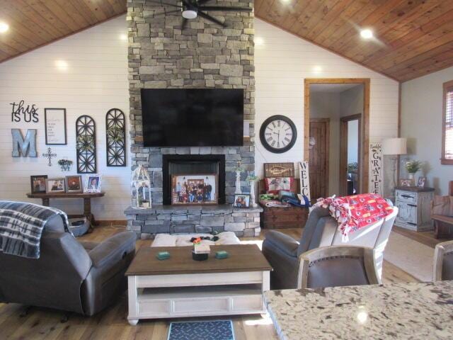 living room featuring a ceiling fan, a fireplace, wood walls, wood finished floors, and wooden ceiling