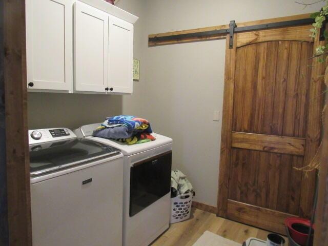 washroom with light wood-style flooring, cabinet space, a barn door, and washing machine and clothes dryer