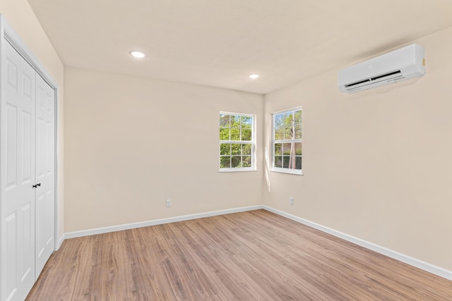 unfurnished bedroom with a wall mounted air conditioner, light wood finished floors, baseboards, and a closet