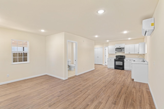 unfurnished living room with a wall mounted AC, light wood-style flooring, baseboards, and a sink