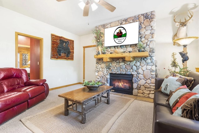 carpeted living room with baseboards, a stone fireplace, and a ceiling fan