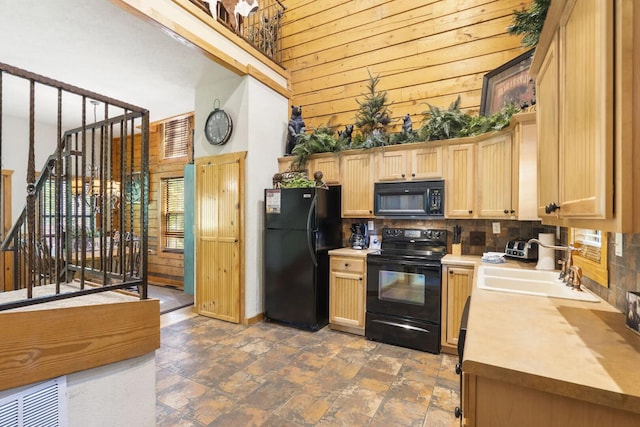kitchen with wooden walls, a high ceiling, light countertops, backsplash, and black appliances