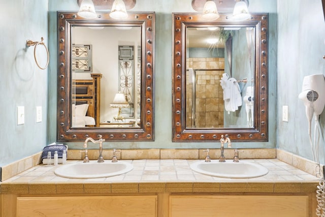 full bath featuring tiled shower, double vanity, and a sink