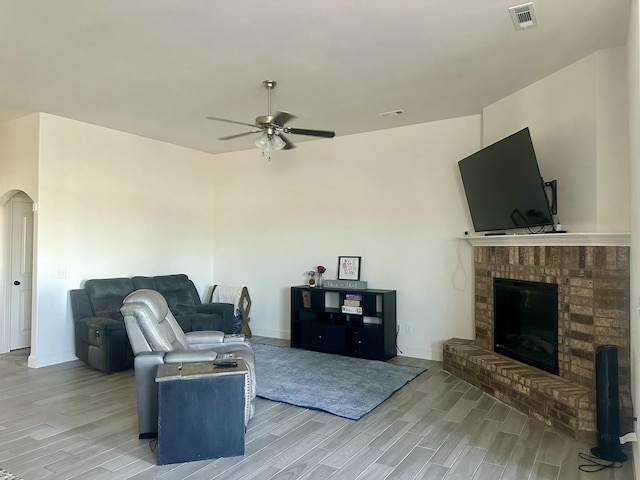living room with a ceiling fan, visible vents, arched walkways, a fireplace, and light wood-style flooring