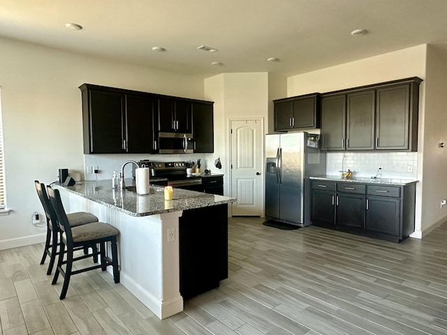 kitchen with a breakfast bar area, appliances with stainless steel finishes, light stone counters, a peninsula, and light wood-style floors