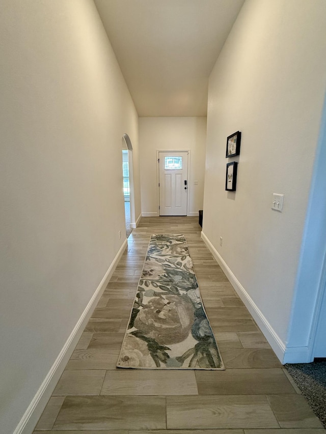 doorway to outside with arched walkways, baseboards, and light wood-type flooring