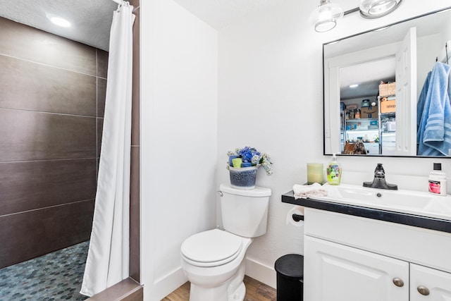 bathroom with toilet, a tile shower, vanity, and wood finished floors
