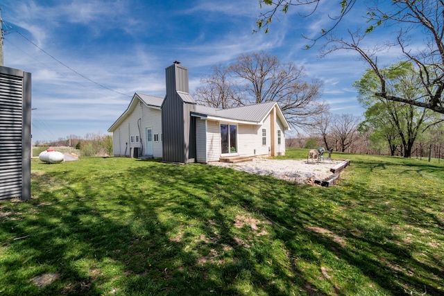 rear view of property with a yard, a patio, metal roof, and a chimney