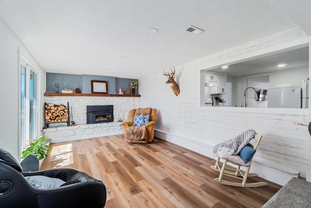 living room featuring a fireplace, visible vents, a textured ceiling, and wood finished floors