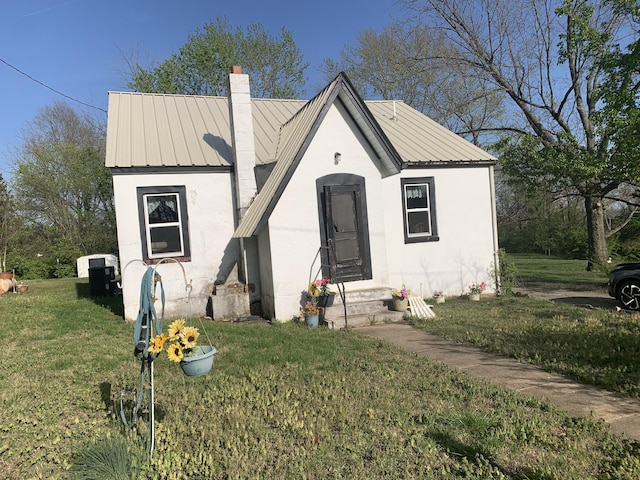 bungalow featuring a front yard, metal roof, and a chimney