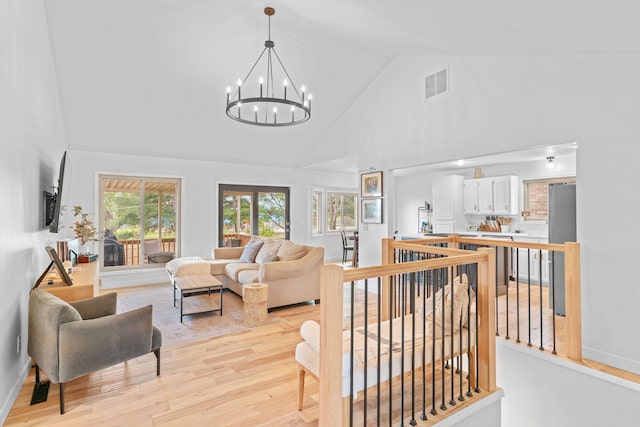 living area with visible vents, baseboards, a chandelier, light wood-style flooring, and high vaulted ceiling