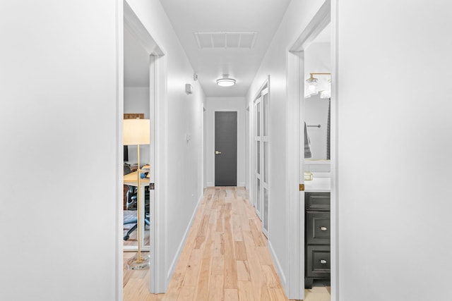 hall with visible vents, light wood-style flooring, and baseboards