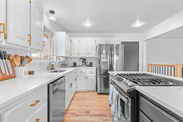 kitchen featuring tasteful backsplash, light wood-type flooring, white cabinetry, appliances with stainless steel finishes, and a sink