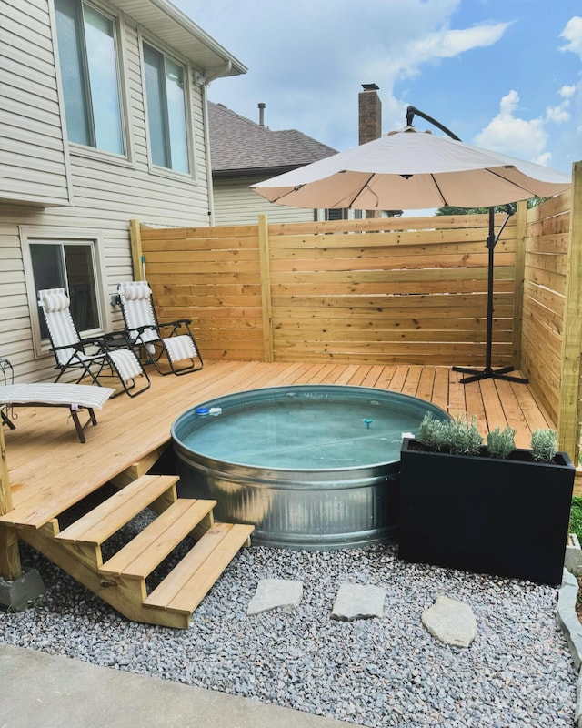 view of pool with a wooden deck, fence, and hot tub deck surround