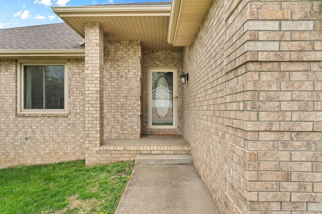property entrance featuring roof with shingles and brick siding
