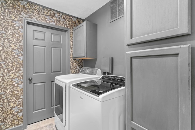 laundry room with wallpapered walls, separate washer and dryer, cabinet space, and visible vents