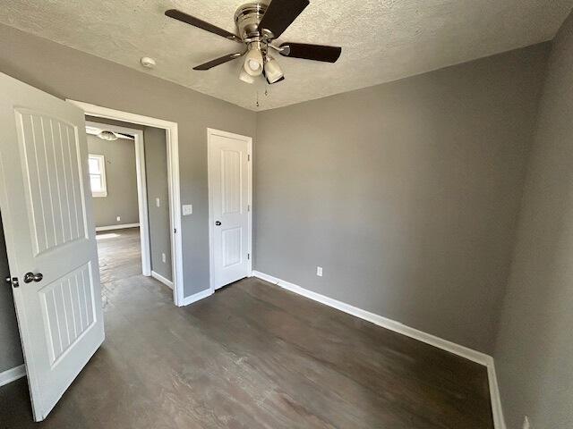 unfurnished bedroom featuring dark wood-style floors, baseboards, a textured ceiling, and ceiling fan