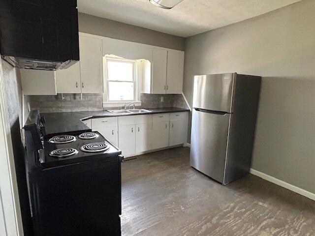 kitchen with a sink, black / electric stove, freestanding refrigerator, and dark countertops