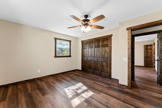 unfurnished bedroom with dark wood-style flooring, a closet, baseboards, and ceiling fan