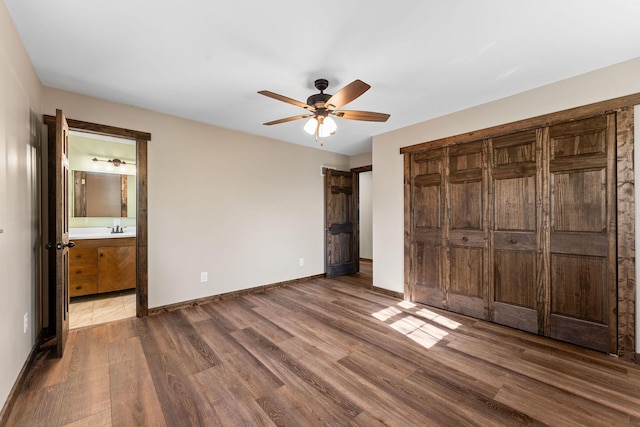 unfurnished bedroom with dark wood-style floors, baseboards, a sink, and ensuite bathroom