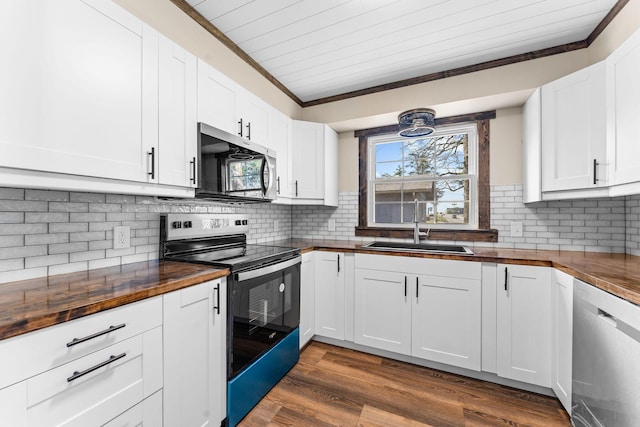 kitchen featuring tasteful backsplash, crown molding, butcher block counters, appliances with stainless steel finishes, and a sink