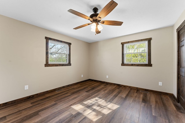 empty room with dark wood-type flooring, a wealth of natural light, a ceiling fan, and baseboards
