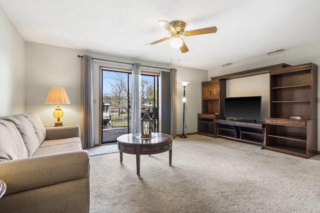 living room featuring a textured ceiling, light colored carpet, baseboards, and ceiling fan