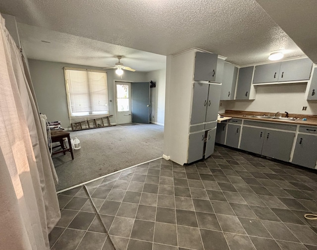 kitchen with a sink, dark carpet, ceiling fan, dark tile patterned floors, and a textured ceiling