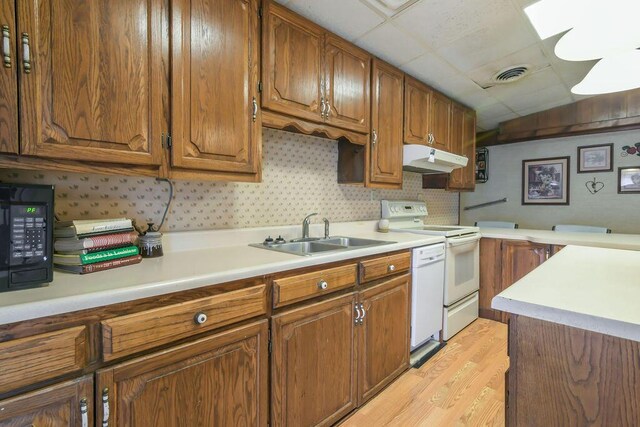 kitchen with white appliances, light countertops, under cabinet range hood, visible vents, and a sink