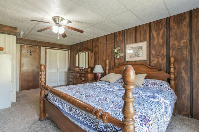 bedroom with wooden walls, a closet, ceiling fan, and carpet flooring