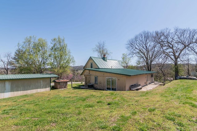 rear view of house with central AC, metal roof, and a lawn