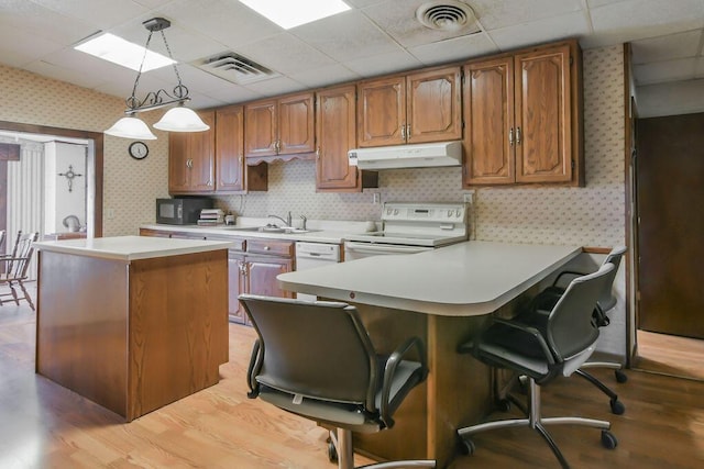 kitchen featuring visible vents, stove, light countertops, under cabinet range hood, and wallpapered walls