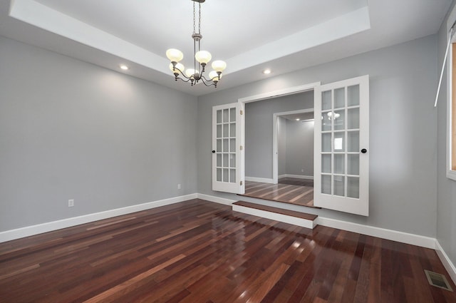 spare room featuring a notable chandelier, baseboards, french doors, dark wood-type flooring, and a tray ceiling