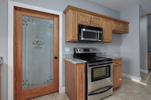 kitchen featuring light tile patterned flooring, baseboards, light stone countertops, and stainless steel appliances