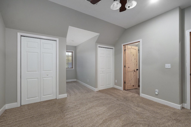 unfurnished bedroom featuring two closets, a ceiling fan, vaulted ceiling, light carpet, and baseboards