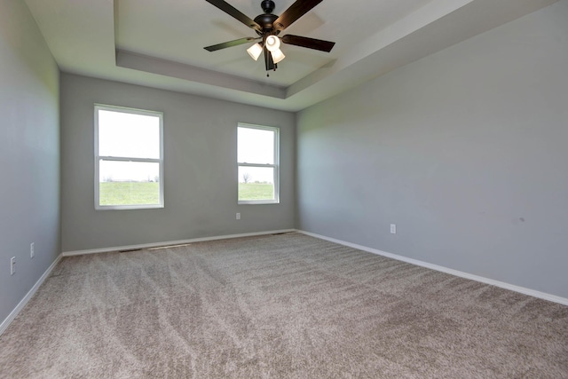 spare room featuring a raised ceiling, baseboards, a ceiling fan, and carpet floors