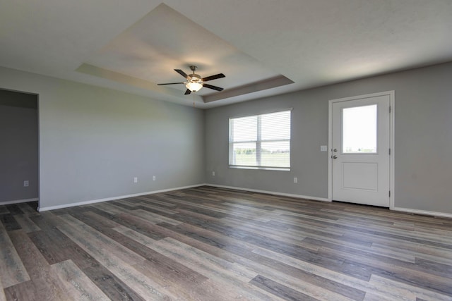 unfurnished room with a tray ceiling, wood finished floors, ceiling fan, and baseboards