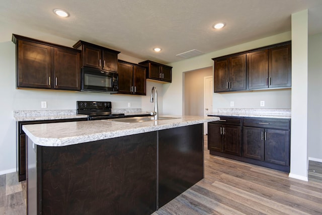 kitchen featuring a sink, light countertops, light wood-type flooring, dark brown cabinetry, and black appliances