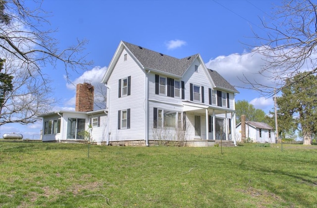 rear view of property with a chimney, covered porch, and a lawn