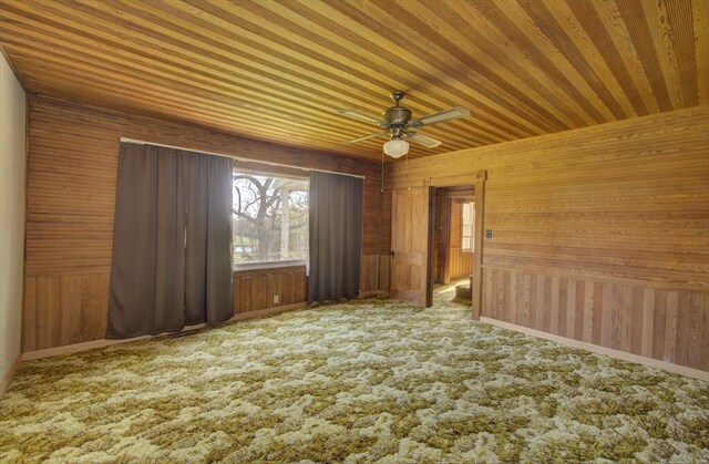 empty room with wooden walls, ceiling fan, baseboards, and carpet