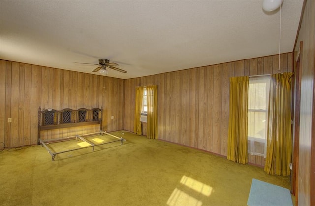 unfurnished bedroom featuring wood walls, multiple windows, carpet flooring, and a textured ceiling