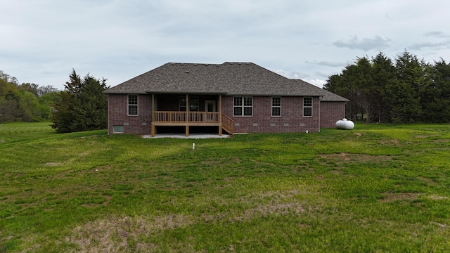 back of house with a lawn, brick siding, roof with shingles, and a deck