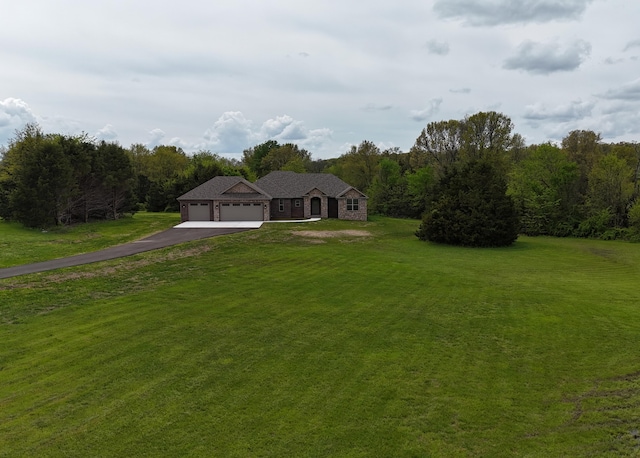 view of front of house featuring a forest view, aphalt driveway, a front yard, and a garage