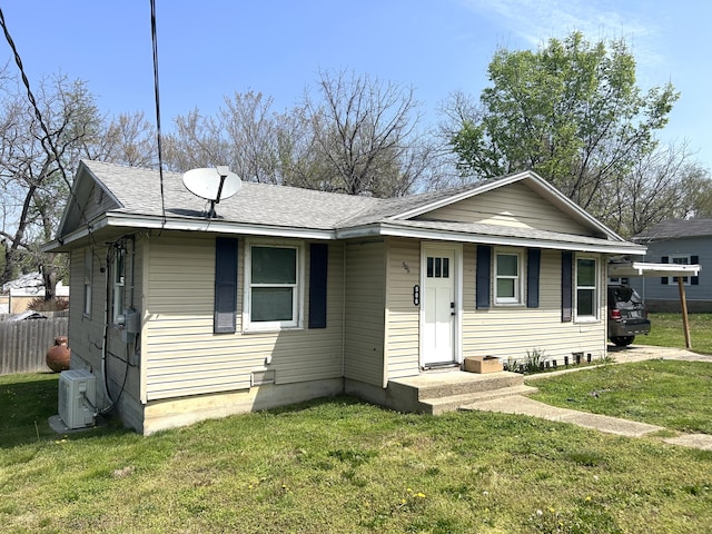 view of front facade featuring ac unit, roof with shingles, a front yard, and fence