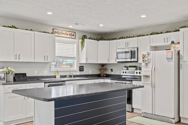 kitchen with recessed lighting, dark countertops, white cabinets, stainless steel appliances, and a sink