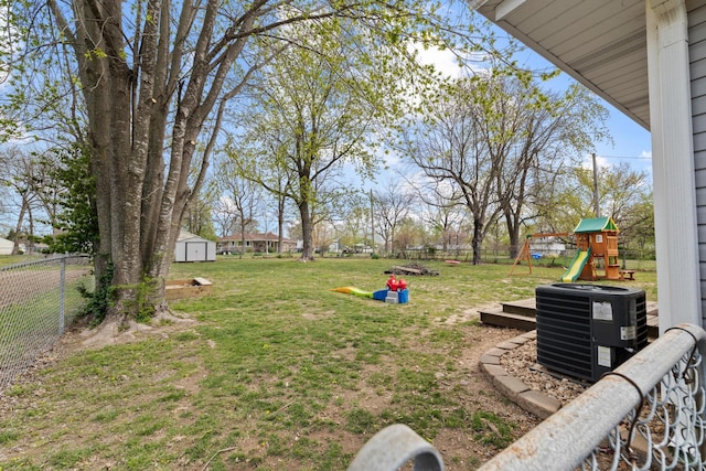 view of yard with central air condition unit, a fenced backyard, an outbuilding, a playground, and a storage unit