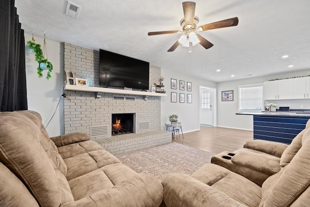 living area featuring recessed lighting, a fireplace, a ceiling fan, visible vents, and wood finished floors